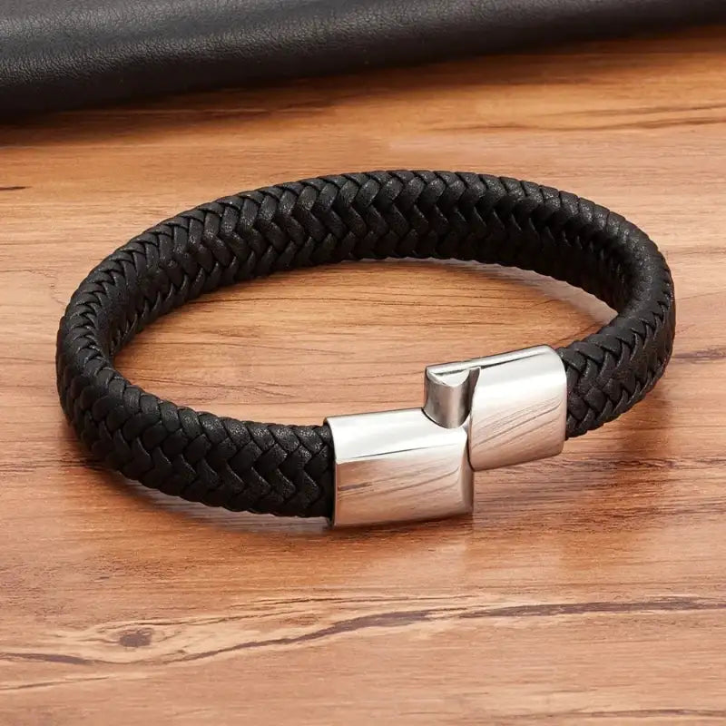 Black braided leather bracelet with a silver clasp on a wooden surface
