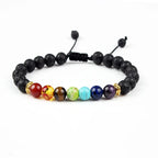 A black lava stone beaded bracelet with seven colorful chakra beads in the center and gold spacer accents, displayed on a clean white background.