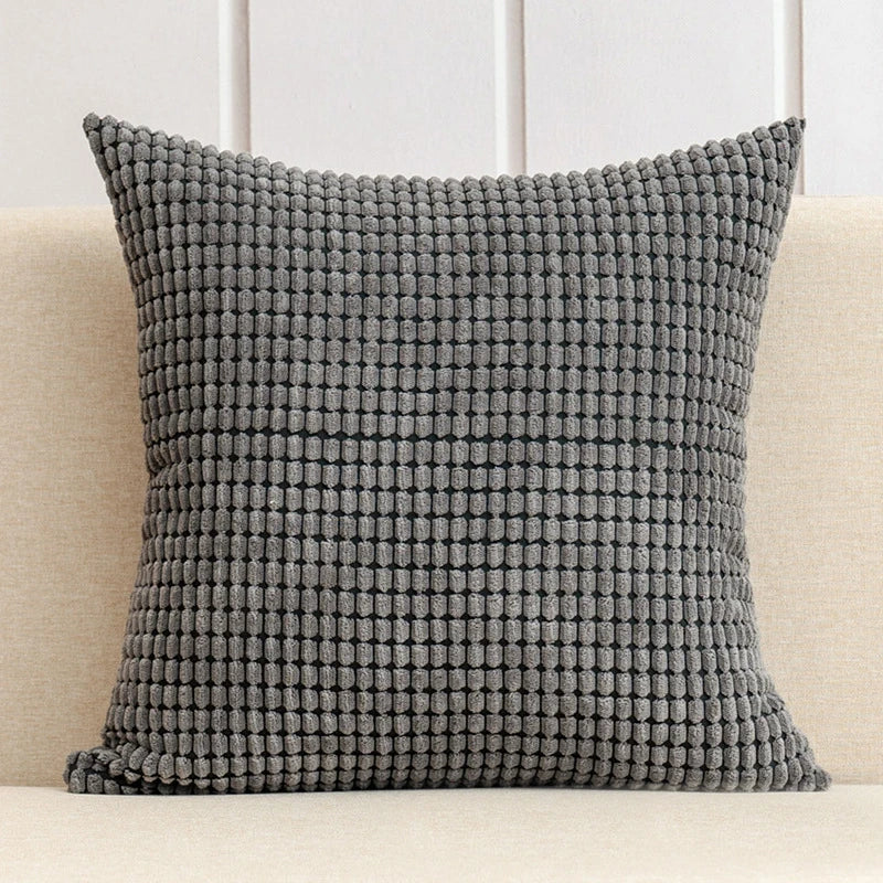 Textured gray pillow on a beige couch with a white paneled wall background