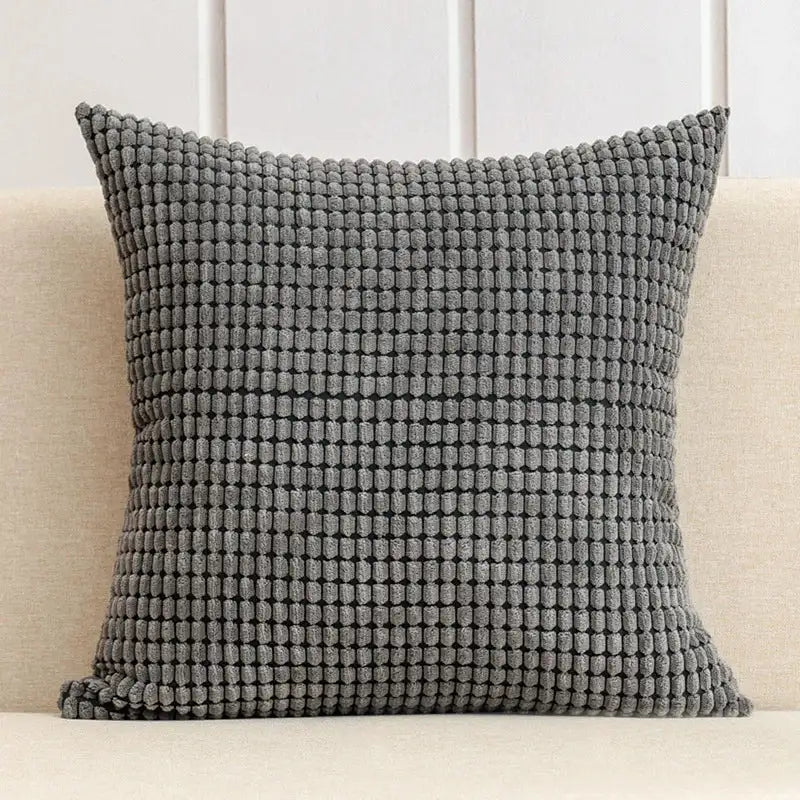 Textured gray pillow on a beige couch with a white paneled wall background
