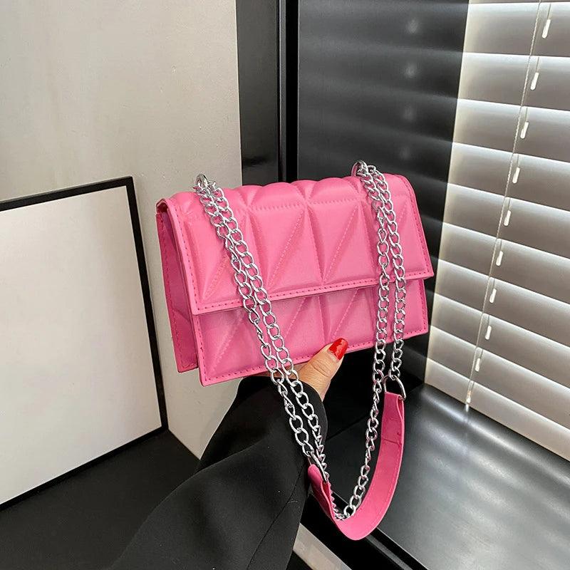 Pink handbag with a chain strap held by a person against a neutral background