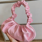 Pink satin handbag held by a hand in front of a glass display case.
