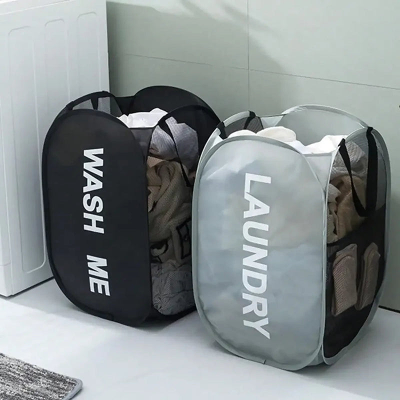 Two laundry bags, one black with 'WASH ME' text and one gray with 'LAUNDRY' text, on a white surface.