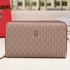 A beige monogram zip-around wallet with a gold-tone logo emblem, displayed on a white surface with a blurred city street background.