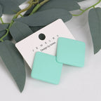 Turquoise square earrings on a white card with 'Jewelry' text, against a leafy green background.
