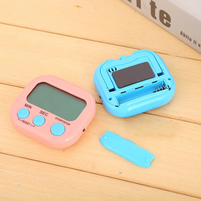 Pink digital kitchen timer with LCD screen and blue control buttons, shown alongside the back of a blue timer with an open battery compartment and removable cover
