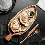 Wooden plate with oysters on a dark surface with cutlery.