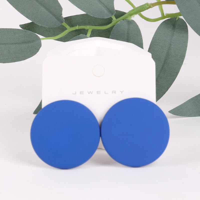 Blue round earrings on a white card with green leaves in the background