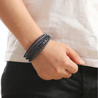 Person wearing a black leather bracelet on a plain background