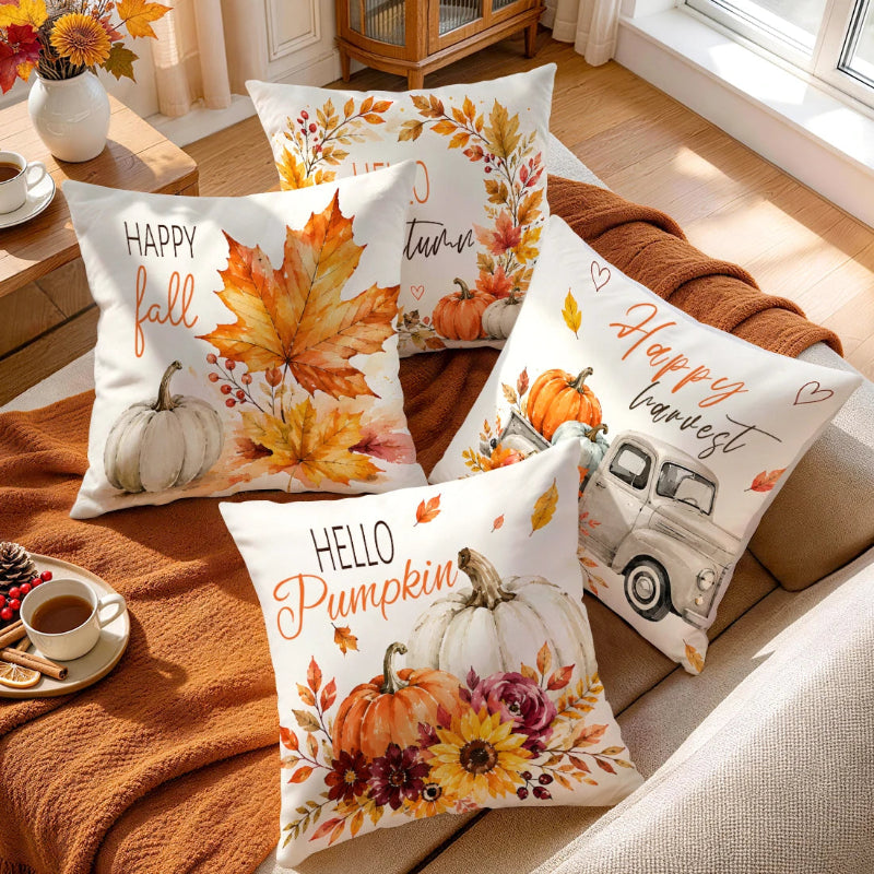 Four decorative throw pillows with autumn watercolor designs are arranged on a beige sofa with a rust-colored blanket. The pillows feature fall leaves, pumpkins, flowers, and phrases like 'Happy fall,' 'turn of the year,' 'Happy harvest,' and 'Hello Pumpkin.
