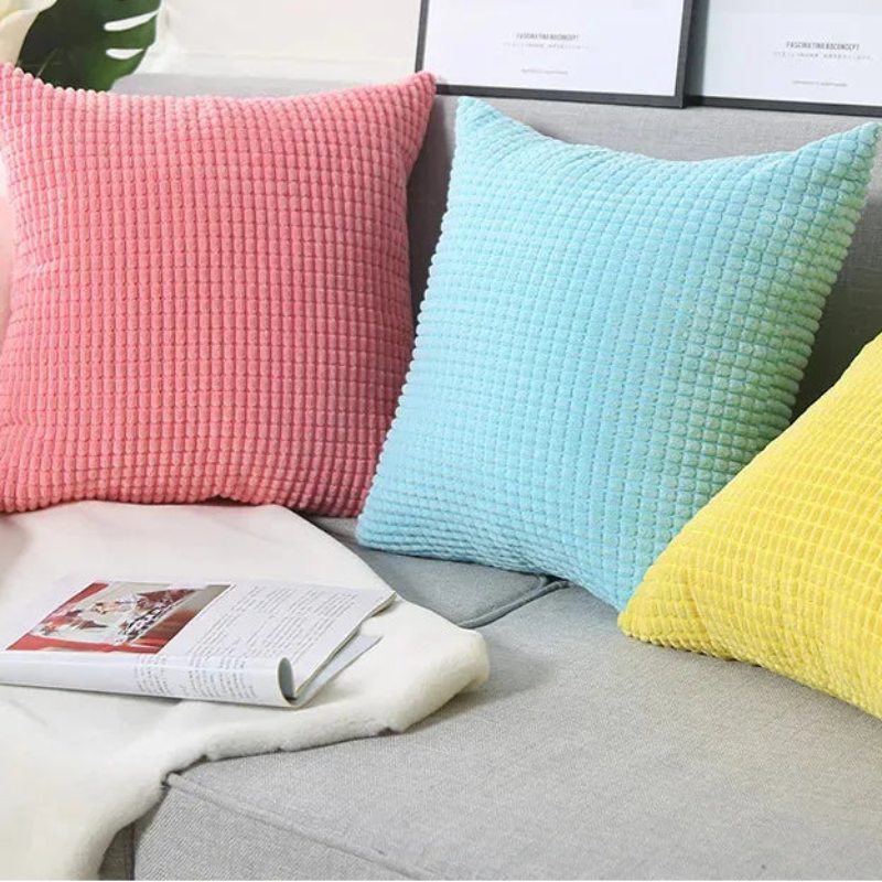 Three colorful pillows on a sofa with a magazine and decorative elements.