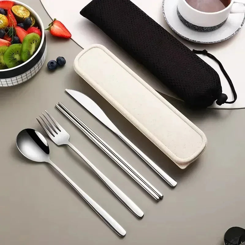 Set of silver cutlery with a case on a table with fruits and a cup.