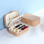 A beige jewelry organizer box shown open and closed on a white surface against a light blue background. The open box contains rings, earrings, and a small red pouch, while the closed box sits beside it.