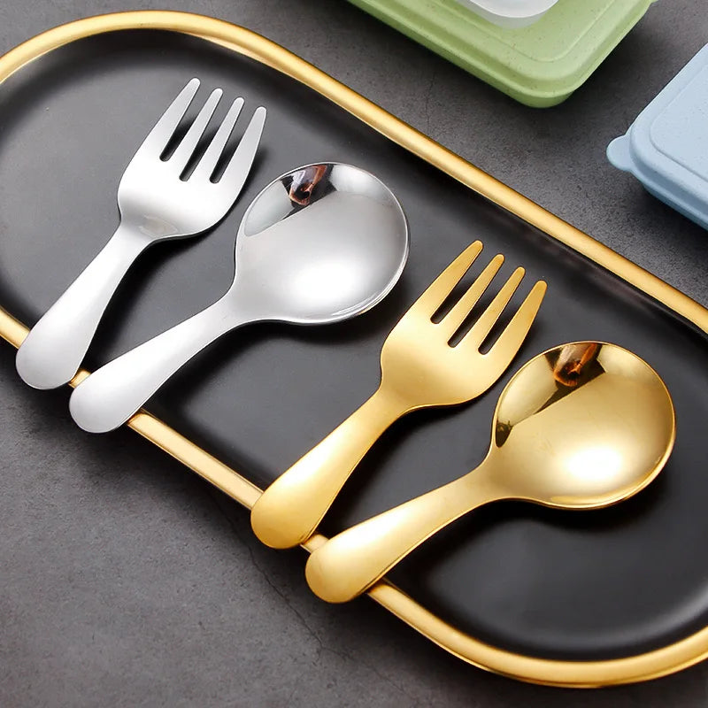 Set of gold and silver cutlery on a black tray with a gold rim.