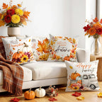 Four autumn-themed throw pillows arranged on a white sofa in a styled living room. The pillows feature fall leaves, pumpkins, flowers, and harvest illustrations, including the phrases 'Hello Pumpkin Hill,' 'Happy Autumn,' and 'Happy harvest.