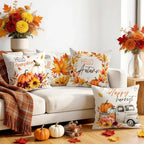 Four autumn-themed throw pillows arranged on a white sofa in a styled living room. The pillows feature fall leaves, pumpkins, flowers, and harvest illustrations, including the phrases 'Hello Pumpkin Hill,' 'Happy Autumn,' and 'Happy harvest.