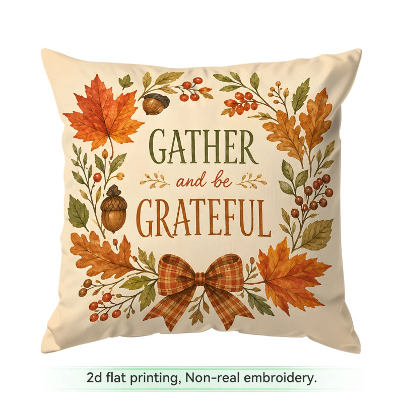 A square cream throw pillow with a fall-themed flat print featuring the text 'GATHER and be GRATEFUL' surrounded by orange and green autumn leaves, acorns, berries, and a plaid bow. Text below reads '2d flat printing, Non-real embroidery.
