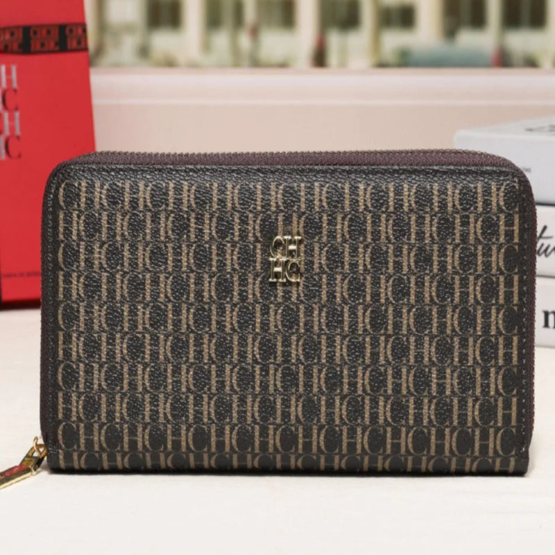A Coach zip-around wallet in the brand's signature monogram canvas, featuring a gold-tone CC turn-lock closure on the front. The wallet is displayed on a white surface with a blurred city street scene in the background.