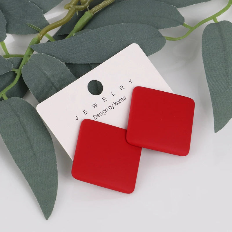 Red square earrings on a white jewelry card with green leaves in the background