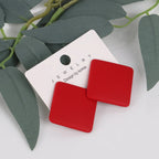 Red square earrings on a white jewelry card with green leaves in the background