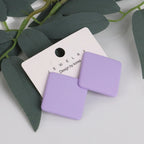 Purple square earrings on a white jewelry card with green leaves in the background