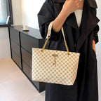 Person holding a beige handbag with a pattern, wearing a black outfit, in an indoor setting.