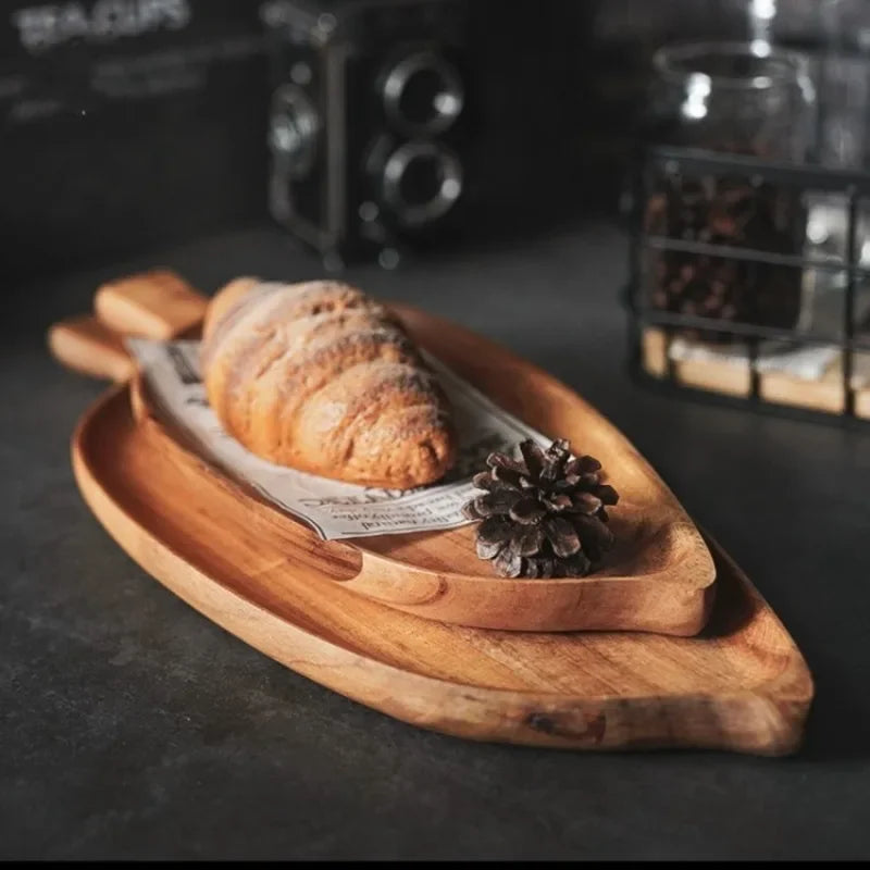 Wooden cutting board with a croissant and knife on a dark surface