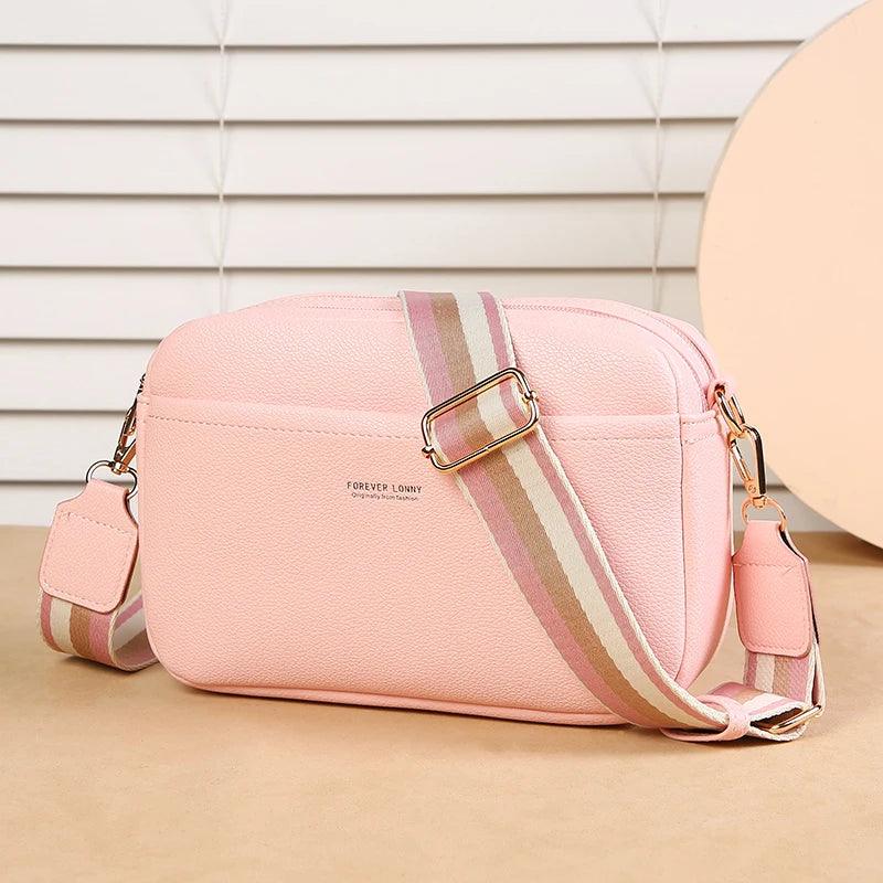 Pink crossbody bag with striped strap on a beige surface
