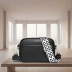 Black crossbody bag with a black and white zigzag strap on a white background