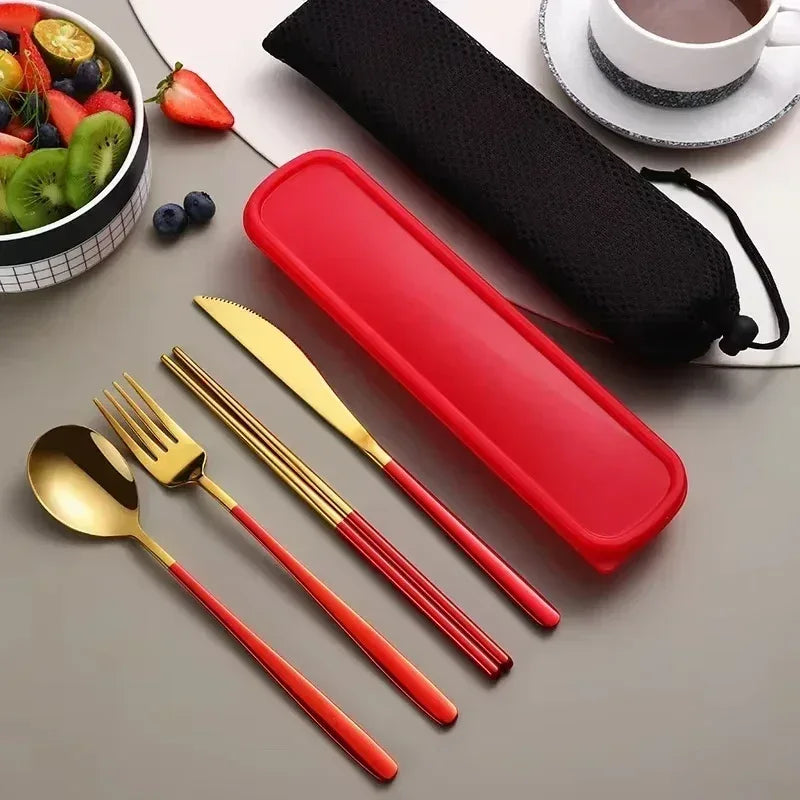 Red and gold cutlery set with a red case on a gray surface, next to a bowl of fruit and a cup.