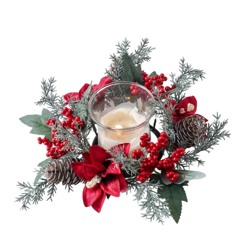 A festive Christmas candle centerpiece in a clear glass holder, surrounded by artificial pine branches, red berries, green leaves, pinecones, and red poinsettia-style flowers on a white background.