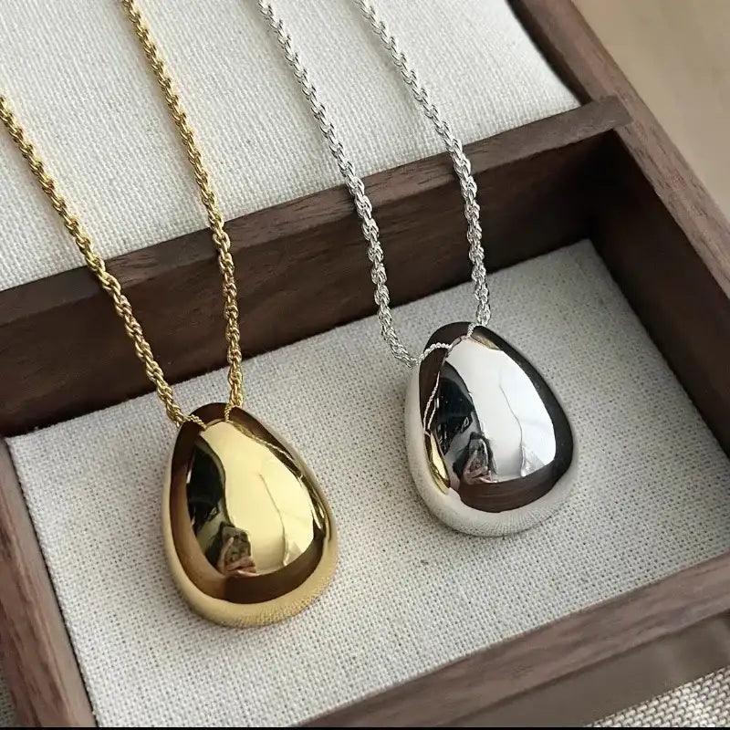 Two necklaces with gold and silver pendants on a textured surface.