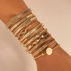Multiple gold bracelets on a wrist against a beige background