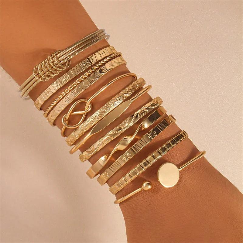 Multiple gold bracelets on a wrist against a beige background
