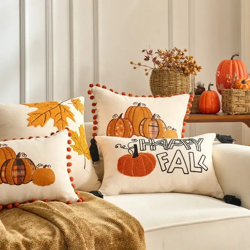 Decorative pillows with pumpkins and 'Happy Fall' text on a sofa, with pumpkins and leaves in the background.