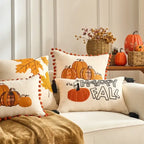 Decorative pillows with pumpkins and 'Happy Fall' text on a sofa, with pumpkins and leaves in the background.