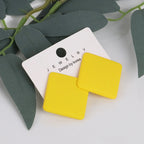 Yellow square earrings on a jewelry card with green leaves in the background