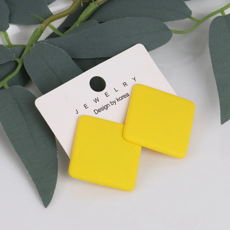 Yellow square earrings on a jewelry card with green leaves in the background