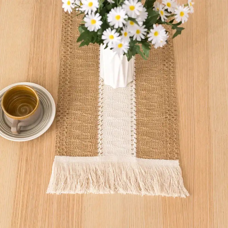 Table setting with a burlap runner, mug, and vase of flowers on a wooden table.