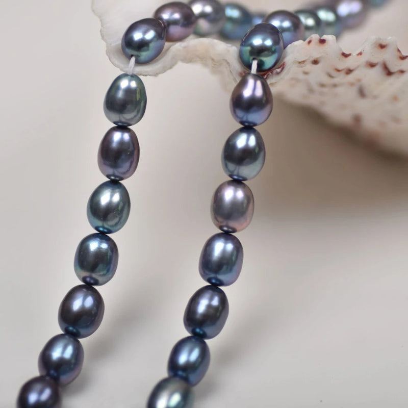 A close-up of a strand of baroque freshwater pearls in a blue-gray iridescent luster, draped over a white seashell on a neutral background.