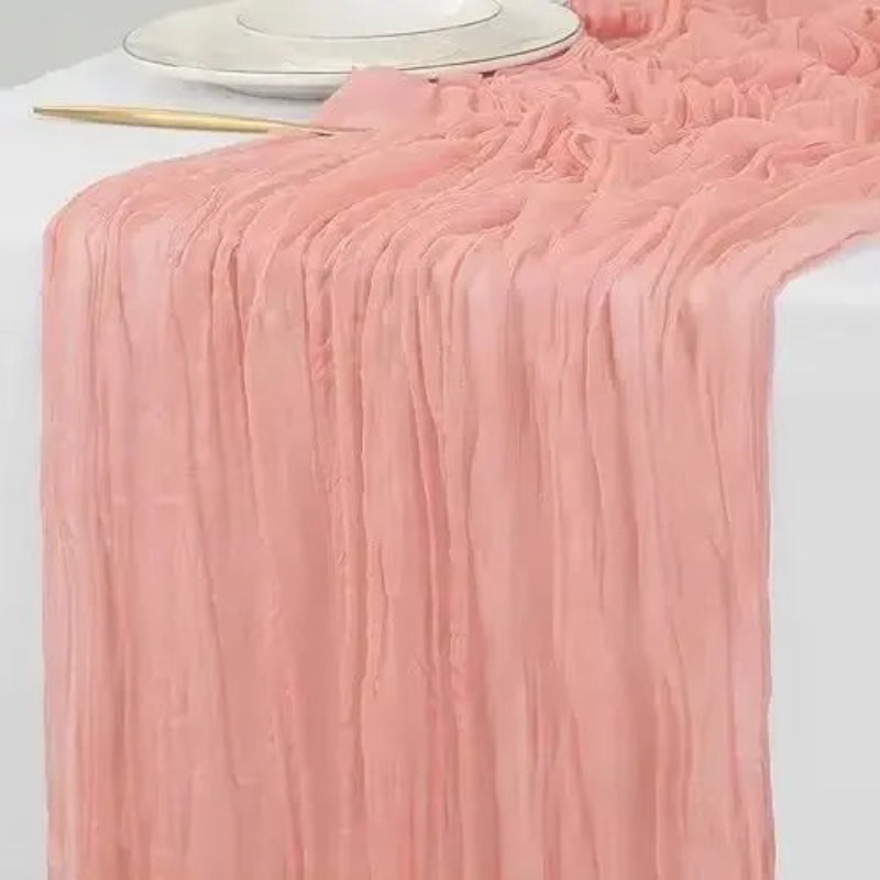 Pink table runner on a white tablecloth with a white plate and gold utensil.