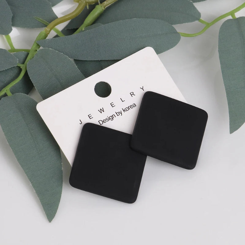 Black square earrings on a 'Jewelry by Korea' tag with green leaves in the background