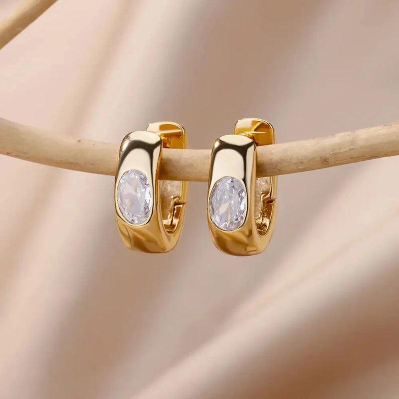 Gold hoop earrings with clear gemstones on a beige background