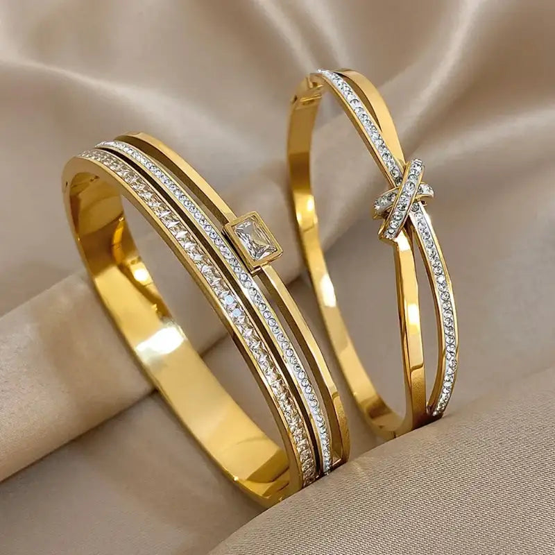 Two gold bangles with diamond accents on a beige fabric background