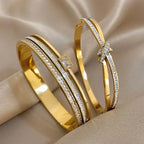 Two gold bangles with diamond accents on a beige fabric background