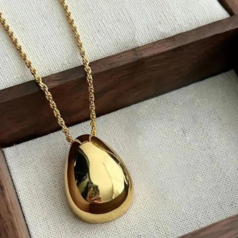 Gold necklace with a teardrop-shaped pendant on a textured surface.