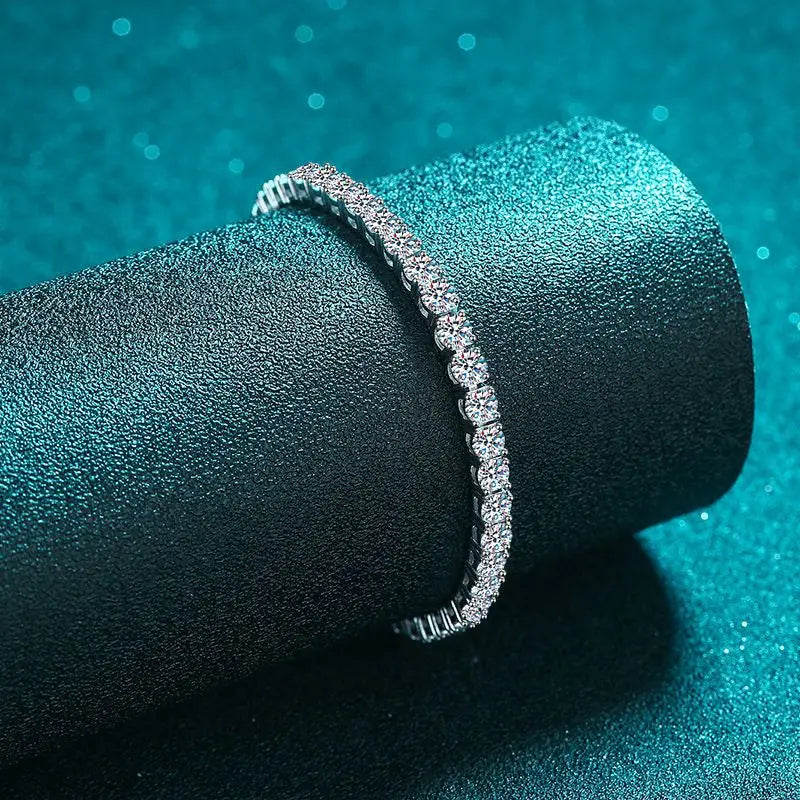 Silver bracelet on a black cylindrical stand against a teal background