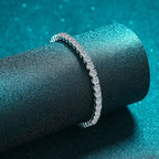 Silver bracelet on a black cylindrical stand against a teal background