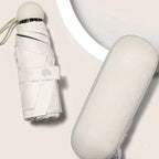 A compact white folding umbrella and its matching hard case, photographed on a clean light beige background.