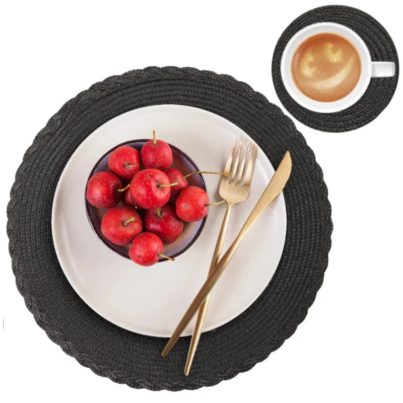 Black woven placemat with a bowl of red apples, gold fork and knife, and a white mug on a white background